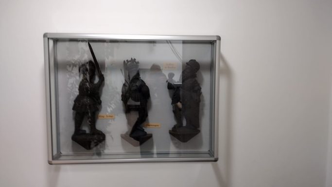 Three abstract sculptures displayed in a glass case on a white wall.