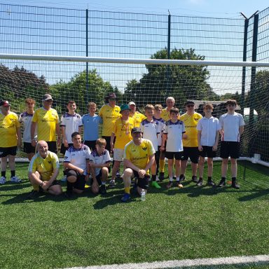 Group of children and adults in football kits pose together on a sunny pitch.