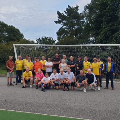 A group of people in yellow and white shirts pose together near a goalpost.