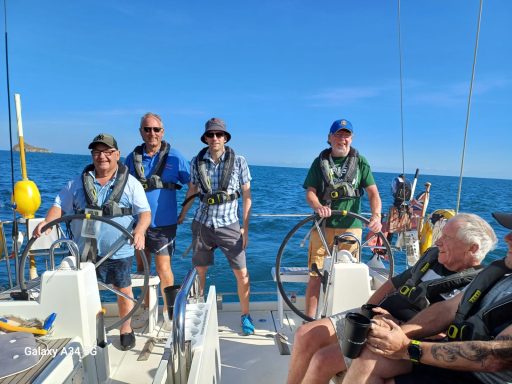 Group of people sailing, smiling, and steering a boat on a sunny day.